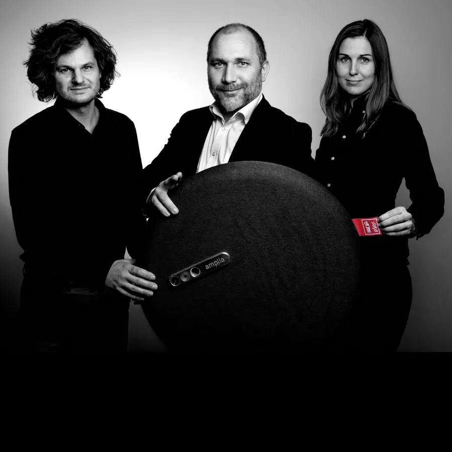 Three Amplla founders photographed in black and white with a black Shield — designer-led portable fire safety.